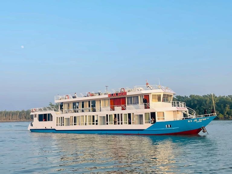M.V. Jol Safari, a white passenger vessel with a blue and red hull, on a calm river with mangrove forest on the far bank