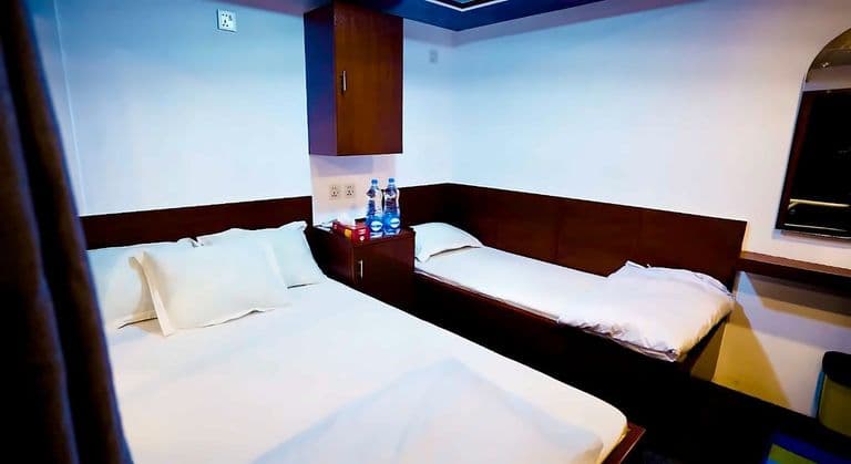 A cabin with a double bed and a second bed beside it, cream curtains and warm ceiling lights