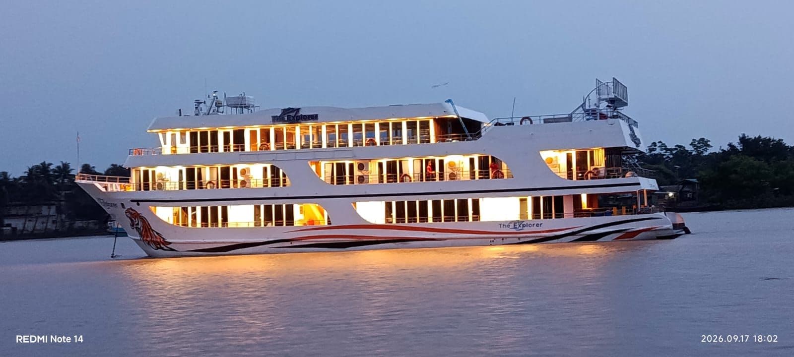 Explorer 1 moored on the river at dusk, all four decks lit, Khulna.